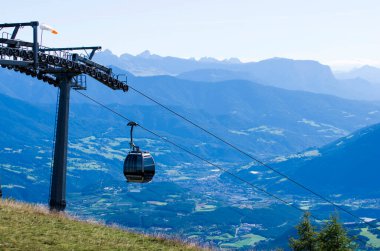 Yaz güneşinin altında mavi gökyüzünde kablo, turistleri güzel çayırları ve ormanlarıyla yüksek dağlara götürüyor.