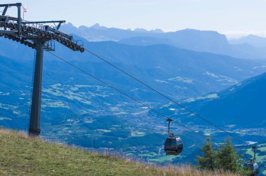 Yaz güneşinin altında mavi gökyüzünde kablo, turistleri güzel çayırları ve ormanlarıyla yüksek dağlara götürüyor.