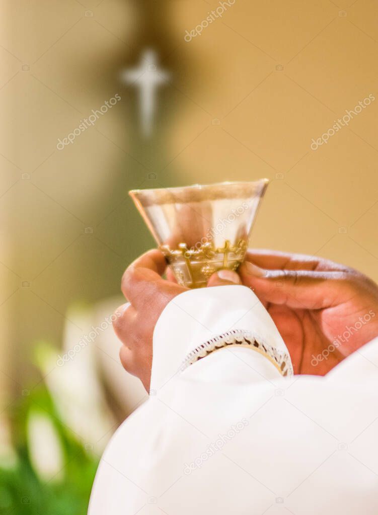 hands of the priest raise the cup containing the blood of Christ, the sacred grail