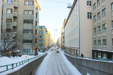 Yol ileri gidiyor. Kışın şehir manzarası. Kaldırımda kar var ve yolun kenarlarında da sarı ve gri evler.