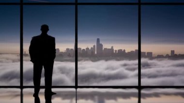 Penceredeki bir adamın silueti bulutların üstündeki şehir siluetine bakıyor.
