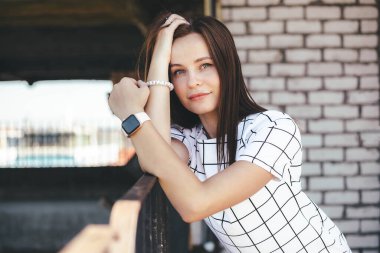 Esmer kadın hafifçe gülümsüyor ve metal çitlere yaslanıyor. Kentsel yaşam tarzı konsepti