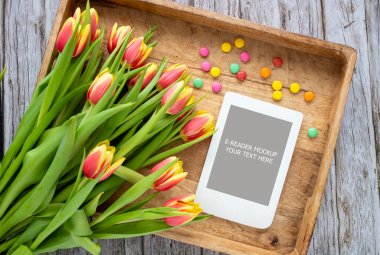 Kırmızı-sarı laleli romantik kompozisyon ve ahşap tepside fotokopi alanı olan e-okuyucu modeli. Kadınsı blog sosyal medya şablonu.