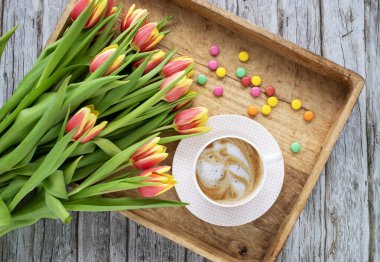 Romantik düz kompozisyon, bir fincan kahve ve ahşap tepside kırmızı ve sarı laleler. Kadınsı blog sosyal medya şablonu.