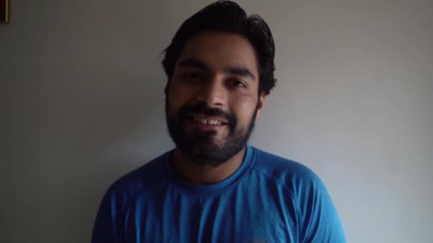 ब्लू शर्ट में दाढ़ीदार भारतीय आदमी कैमरा के सामने मुस्कुराते हुए मध्यम बंद — स्टॉक वीडियो
