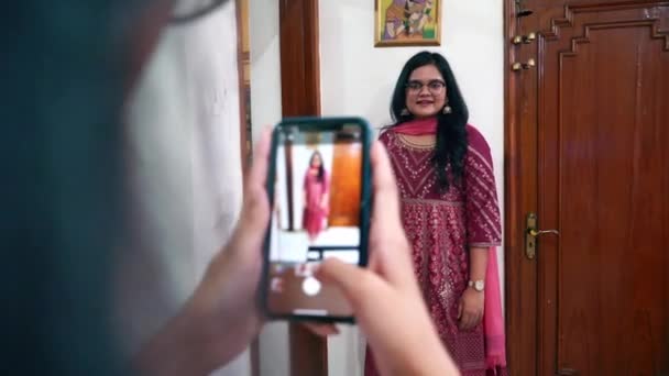 Mano di una ragazza che tiene lo smartphone scattare una foto completa del corpo del suo amico che indossa abiti rosa rosa Saree all'interno della casa in Agra, India - Medium Shot — Video Stock