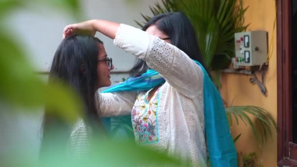 Młoda Hinduska dziewczyna z niebieskim szalikiem dotykająca długich, czarnych włosów swojej przyjaciółki rozmawiając ze sobą przed domem w Agra, Indie - średni strzał, wolny ruch — Wideo stockowe