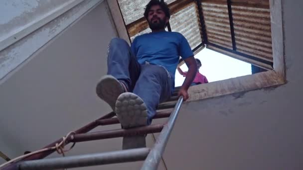 A Bearded Man Descending Facing Away From A Metal Ladder With A Young Girl Looking Down At Him While Standing In Attic In Agra, India - High-Angle Shot — Stock Video