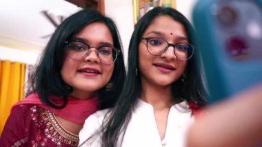 Geleneksel elbiseli ve gözlüklü iki Hintli genç kız Agra, Hindistan 'daki evinde akıllı bir telefonla selfie çekiyorlar.