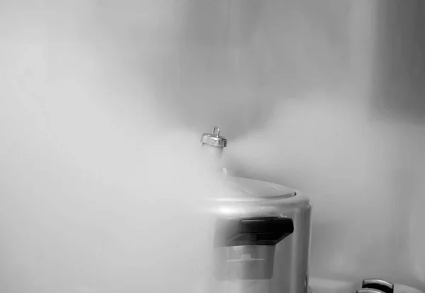 Pressure cooker on the stove releasing steam, black and white photography.