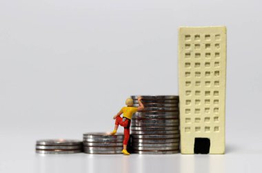 Minyatür bir kadın bozuk para yığınına basarak minyatür bir binaya tırmanmaya çalışıyor. Kadınların terfisinin zorluğu kavramı.