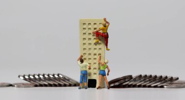 Minyatür insanlar madeni paralarla minyatür bir binaya tırmanmaya çalışıyorlar. İş sıkıntısının derinleşmesi kavramı.