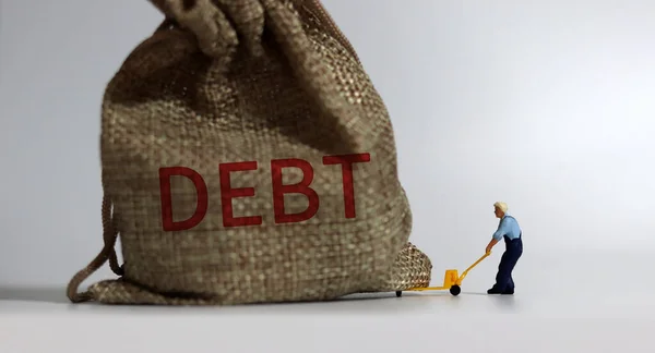 Debtという単語を持つバンドルをドラッグするミニチュアの男 過剰債務のリスクに関する概念 — ストック写真