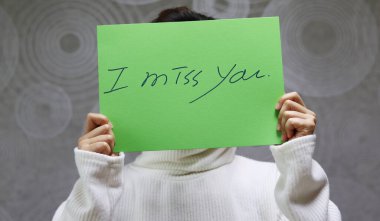 Beyaz kazak giyen bir kadın el yazısıyla yazılmış bir karaktere sahiptir. El yazısıyla yazılmış bir mektup, seni özledim.