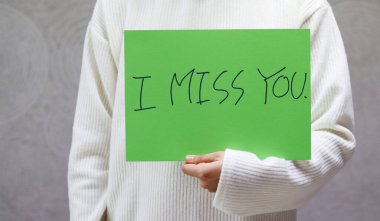 Beyaz kazak giyen bir kadın el yazısıyla yazılmış bir karaktere sahiptir. El yazısıyla yazılmış bir mektup, seni özledim.