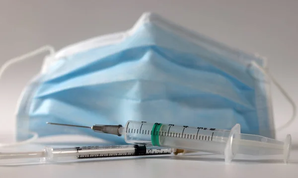 A mask and two disposable syringes. Concept of wearing a mask and the importance of vaccination.