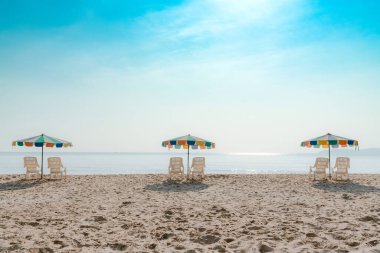 Mavi gökyüzü olan tropikal plajda beyaz plaj koltuğu ve şemsiye