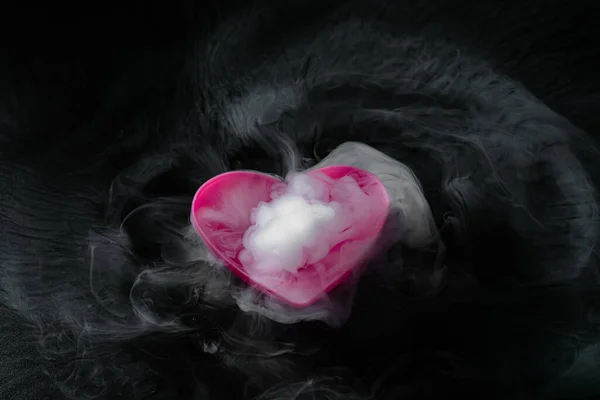 smoke of dry ice with pink heart shaped cup isolated on black background