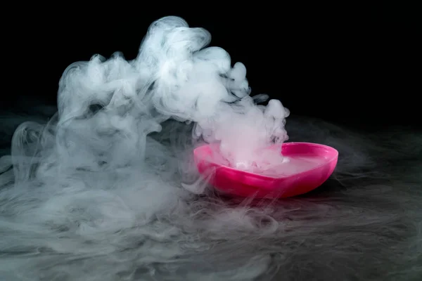 smoke of dry ice with pink heart shaped cup isolated on black background