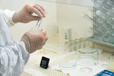 Scientist in protective white coat, mask and gloves analyzes a virus or bacteria sample in a laboratory with vials, glass flasks and chemicals. Medical lab test, new vaccine research or development