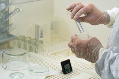 Scientist in protective white coat, mask and gloves analyzes a virus or bacteria sample in a laboratory with vials, glass flasks and chemicals. Medical lab test, new vaccine research or development