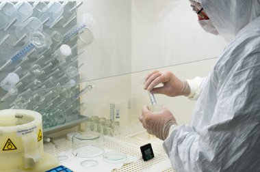 Scientist in protective white coat, mask and gloves analyzes a virus or bacteria sample in a laboratory with vials, glass flasks and chemicals. Medical lab test, new vaccine research or development