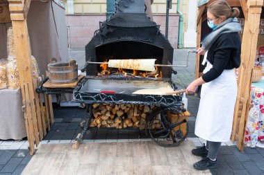 Vilnius, Litvanya - 20 Eylül 2020: Sakotis 'i hazırlayan ya da pişiren maskeli kız, Litvanya mutfağı ve Polonya geleneksel pasta katmanlı pasta, markette ya da ateşte Noel bisküvisi