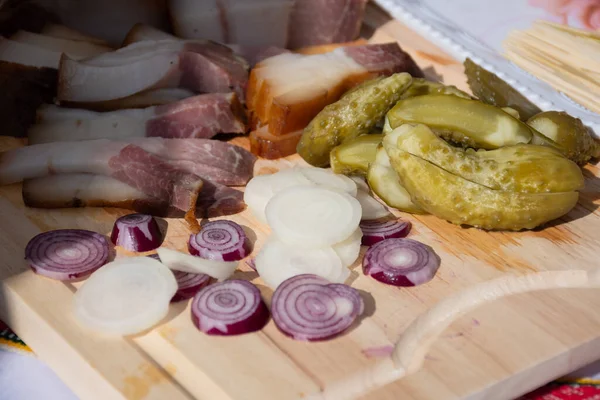 Wooden board filled with starters, appetizers and snacks, food for a feast celebration, Lithuanian or Northern Europe or Baltic food, slices of meat, onions and cucumbers