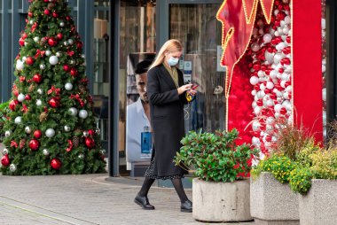 Vilnius, Litvanya - 11 Kasım 2020: Maske takan güzel sarışın kız Covid veya Coronavirus salgını sırasında bir mağaza veya alışveriş merkezi yakınında yürüyor, Noel geçmişi
