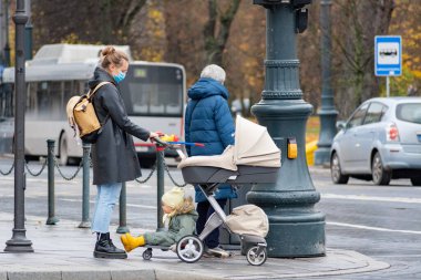 Vilnius, Litvanya - 6 Kasım 2020: Bebek arabalı kız Covid veya Coronavirus salgını sırasında bir dükkan veya alışveriş merkezi yakınlarında yürüyor