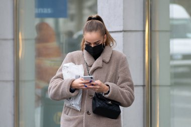 Vilnius, Litvanya - 6 Kasım 2020: Covid ya da Coronavirus acil durumu sırasında akıllı telefondan uygulamayı kontrol eden maskeli kız ya da kadın. 