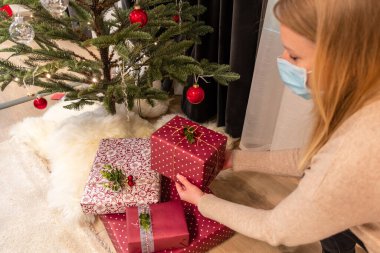 Vilnius, Litvanya - 15 Kasım 2020: Maske takan güzel sarışın kız Noel ağacını süslüyor ve evde hediyeler hazırlıyor