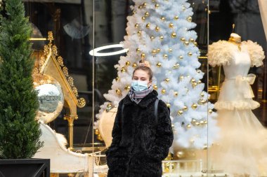 Vilnius, Litvanya - 22 Kasım 2020: Maske takan güzel sarışın kız Covid veya Coronavirus salgını sırasında bir mağaza veya alışveriş merkezi yakınında yürüyor, Noel geçmişi