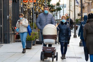 Vilnius, Litvanya - 22 Kasım 2020: Bebek arabalı koruyucu maskeli çift Noel ve Covid veya Coronavirus salgını sırasında şehirde bir dükkan veya alışveriş merkezi yakınlarında yürüyor