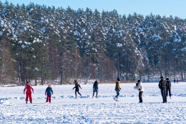 Vilnius, Litvanya - 19 Ocak 2021: Arka planda karla kaplı bir orman ağaçlarıyla donmuş bir gölde kayak yapan insanlar 
