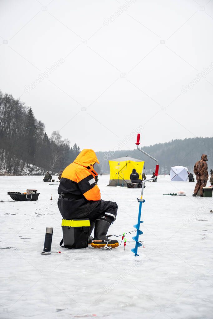 Fisherman fishing on a frozen lake in winter with fishing pole or rod, ice auger and equipment for fishing, vertical