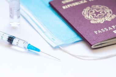 İğne, şişe, cerrahi yüz maskesi ve pasaport ya da vizeyle beyaz bir masada kullanılmaya hazır bir şırınga. Covid ya da Coronavirus aşısı arka planı