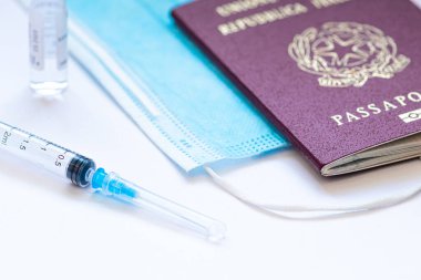 İğne, şişe, cerrahi yüz maskesi ve pasaport ya da vizeyle beyaz bir masada kullanılmaya hazır bir şırınga. Covid ya da Coronavirus aşısı arka planı