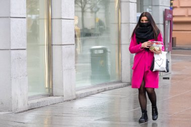 Vilnius, Litvanya - 5 Mart 2021: Maske takan ve Covid veya Coronavirus salgını sırasında alışveriş merkezi yakınlarında yürüyen güzel bir kız