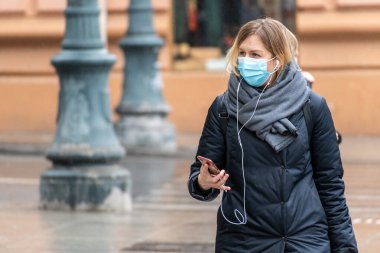 Vilnius, Litvanya - 5 Mart 2021: Covid veya Coronavirus acil durumu sırasında sokakta maske ve akıllı telefonla yürüyen kız veya kadın 