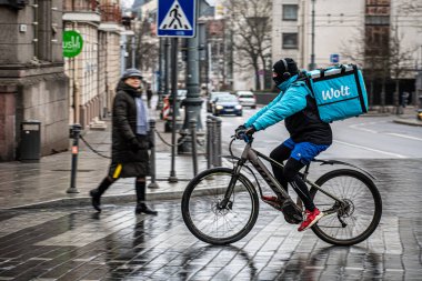 Vilnius, Litvanya - 5 Mart 2021: Wolt için çalışan bisikletli ve maskeli bir sürücü, mobil bir uygulama üzerinden sipariş veren çevrimiçi gıda siparişi ve dağıtım hizmeti