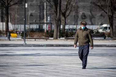 Moscow, Russia - March 9 2021: Man or boy with mask and ushanka or fur cap walking in the city center during Covid or Coronavirus outbreak clipart