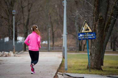 Sarışın kız şehirde koşuyor ya da kulaklıkla ya da kulaklıkla koşuyor.