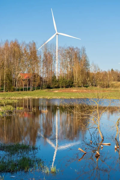 Wind turbine near a forest and lake with clear blue sky on background. Renewable energy concept, green ecological energy generation. Energy industry. Vertical