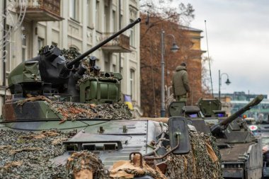 Taretlerinde askerler olan zırhlı tanklardan oluşan bir sütun ve yola doğru ilerleyen bir otomatik top.