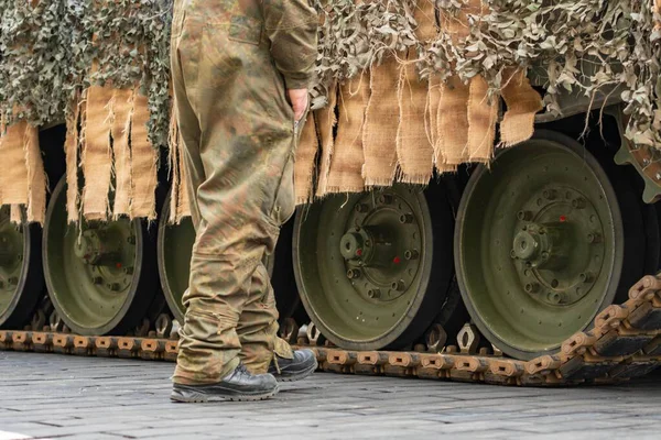 Askeri kamuflajlı asker zırhlı bir leoparın yanında yürüyor.