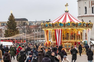 Vilnius, Litvanya - 30 Kasım 2025: Vilnius, Litvanya, Avrupa 'da bir festival şehir meydanında atlıkarıncalı parlak ışıklı bir Noel ağacı, insanlarla çevrili, tatil ışıkları ve market tezgahları