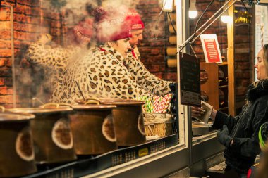 Vilnius, Litvanya - 3 Aralık 2025: Sıcak şarap ve sıcak çikolata satan bir satıcı Vilnius Noel pazarında, sıcak tencere ve sıcak tatil ışıklarıyla çevrili 