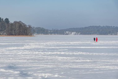 Karlı bir günde karlı ağaçlarla çevrili donmuş bir gölde kışın tadını çıkaran bir çift.