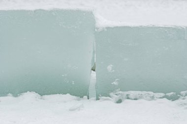 Taze beyaz kar üzerinde dinlenen şeffaf buz bloklarının yer aldığı soyut kış sahnesi, donmuş dokular, serin tonlamalar ve soğuk açık havada minimalist doğal formlar sergiliyor.